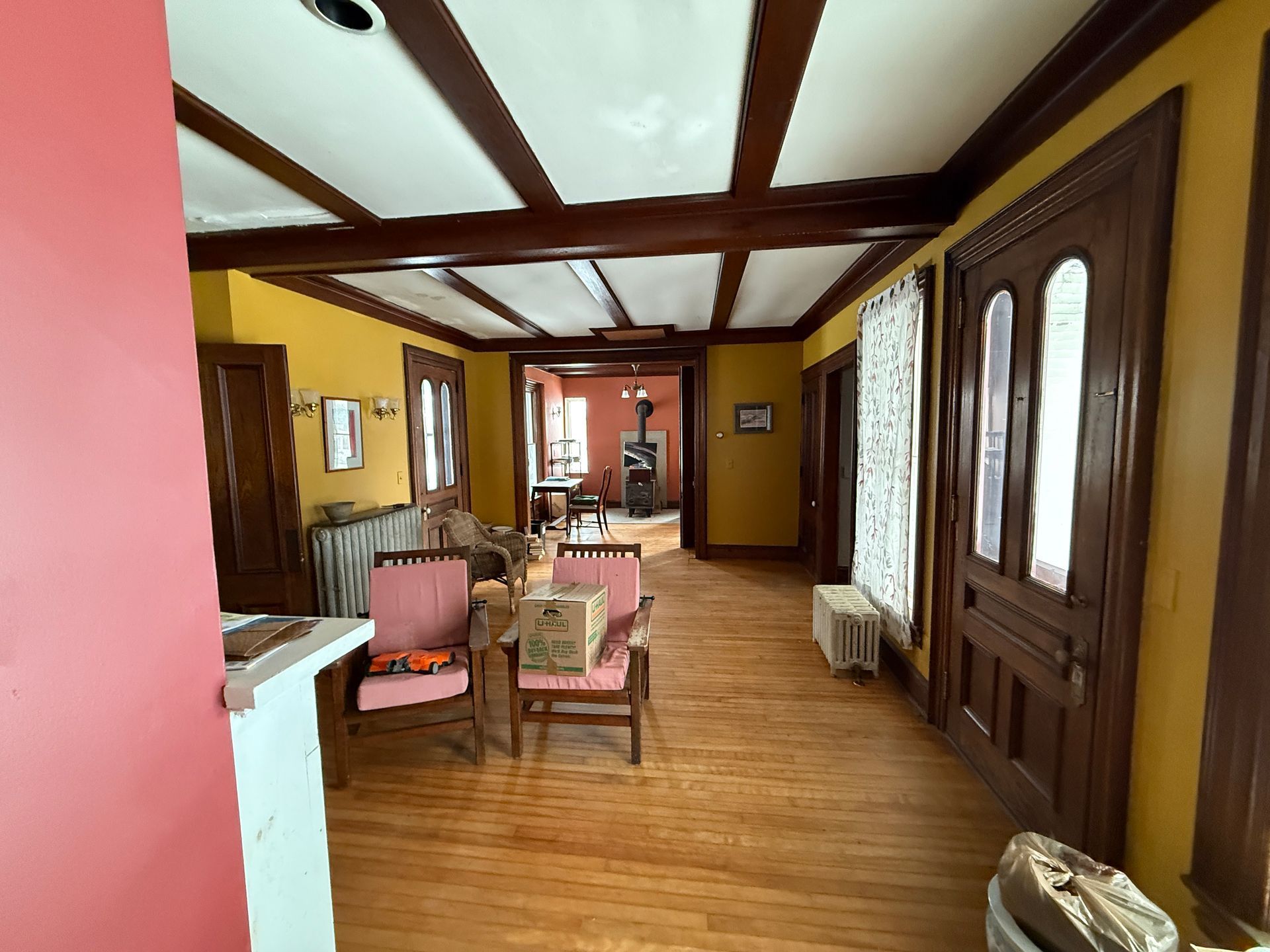 Interior view of a room with exposed wooden beams, yellow walls, and hardwood floors. Furnishings are visible.