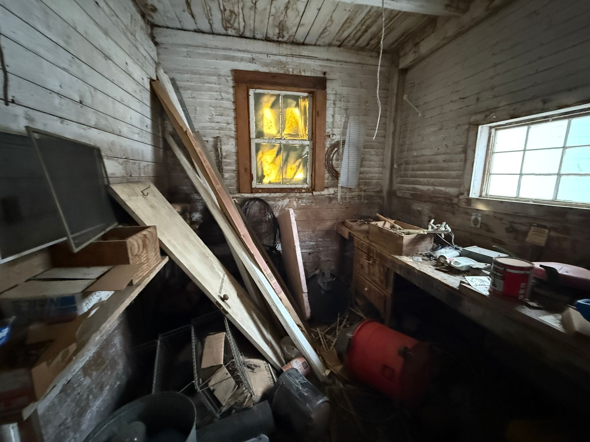 Interior of a small, shed with a workbench and materials. Two windows illuminate the space.