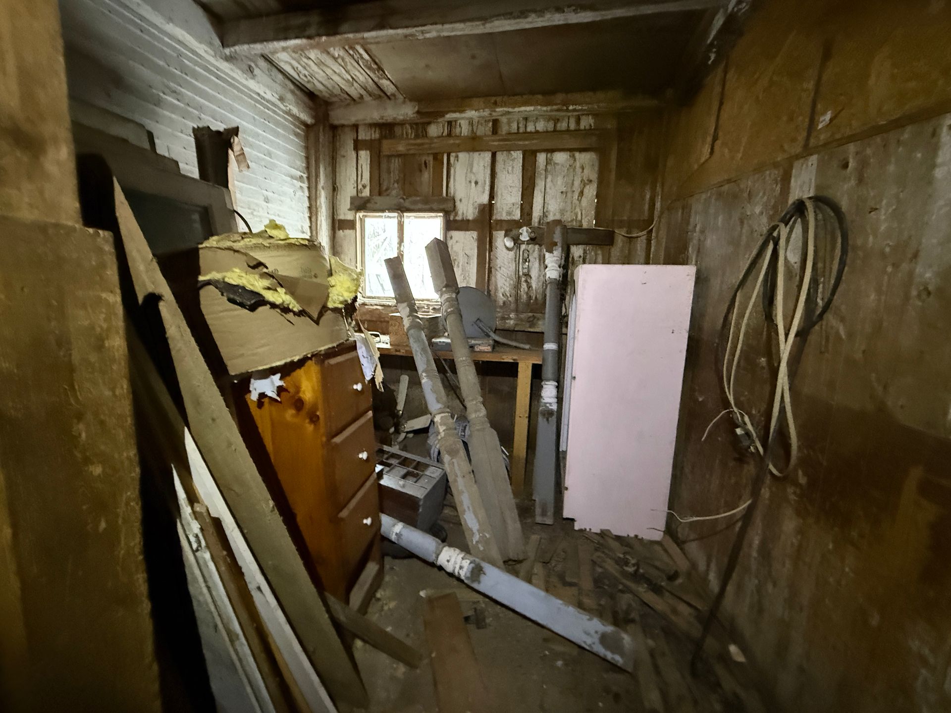 Interior of a shed with wood walls and various items including a dresser, pink panel, and tools.