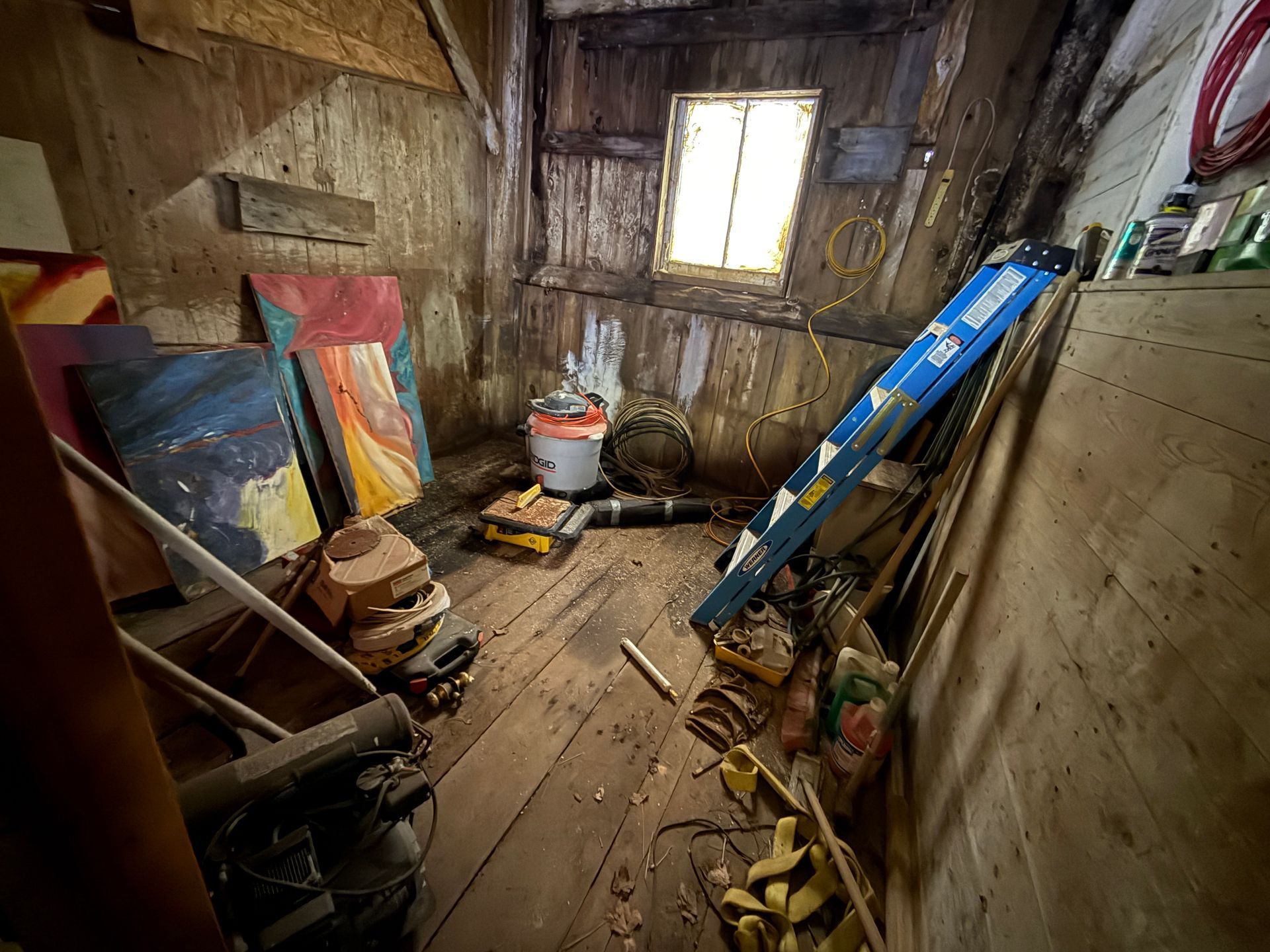 Wooden room with artwork, ladder, tools, and a window.