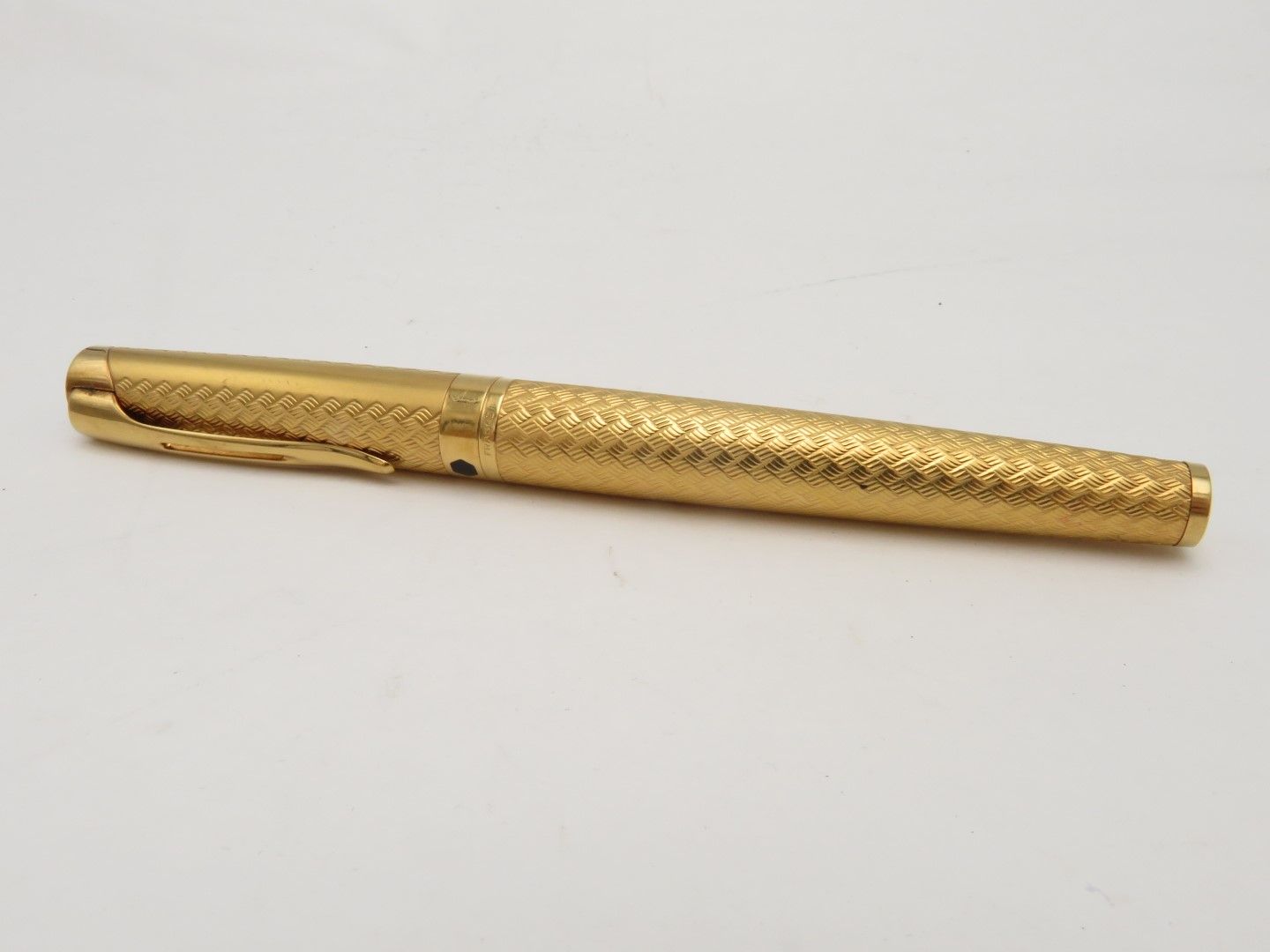 Gold-colored pen with intricate textured pattern; lying on a white surface.