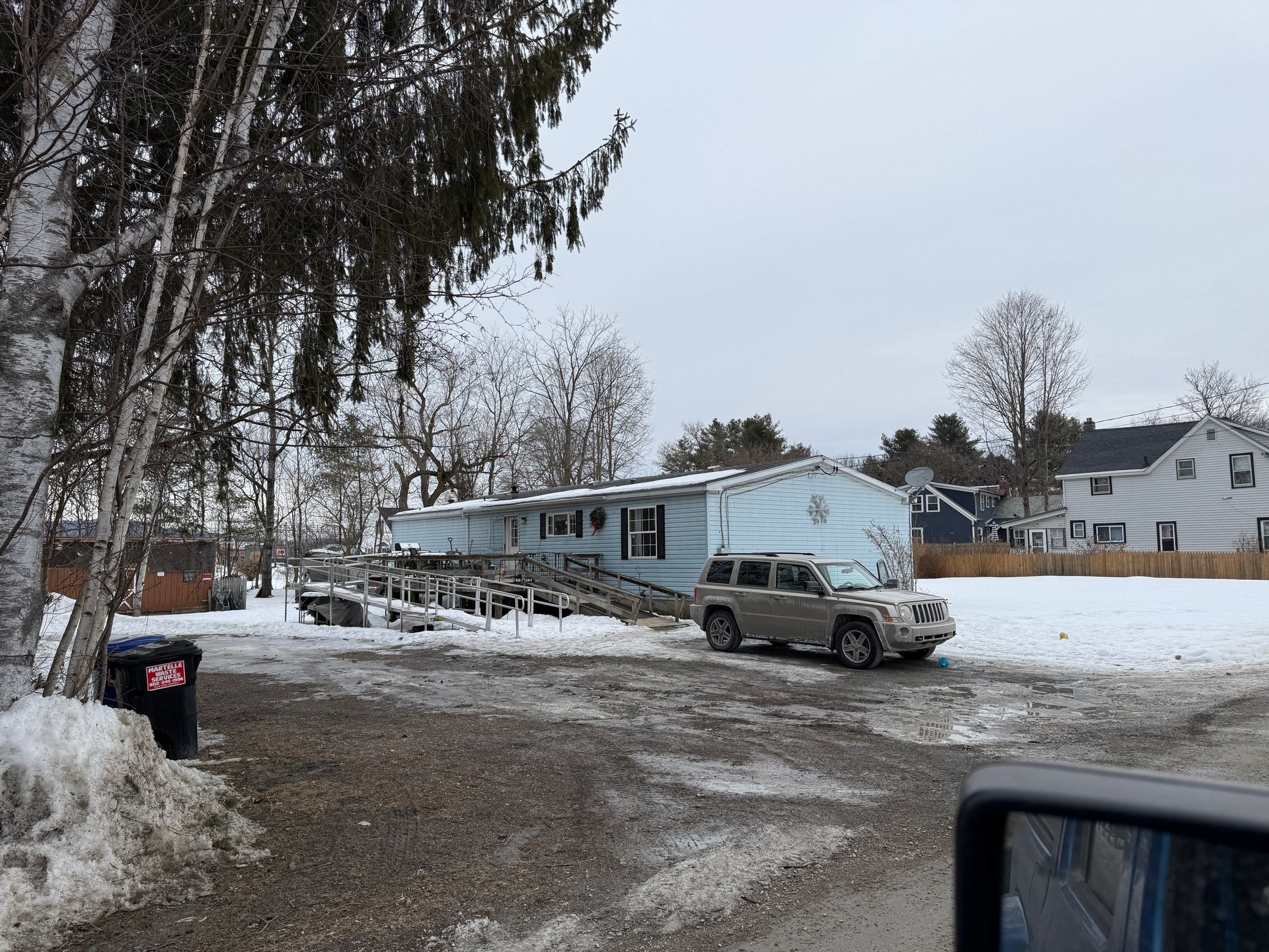 A light blue mobile home with a car parked in front, on a snowy day.