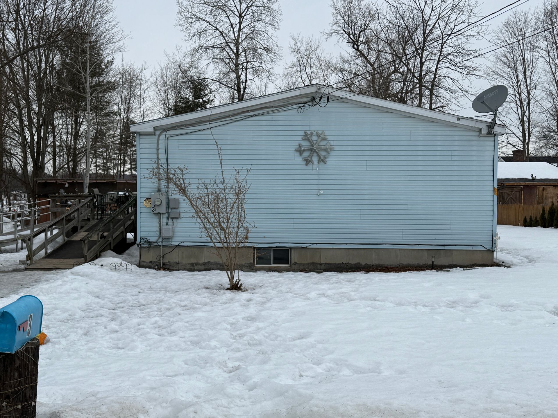 A light blue house with a snow-covered yard; a mailbox and ramp are visible.