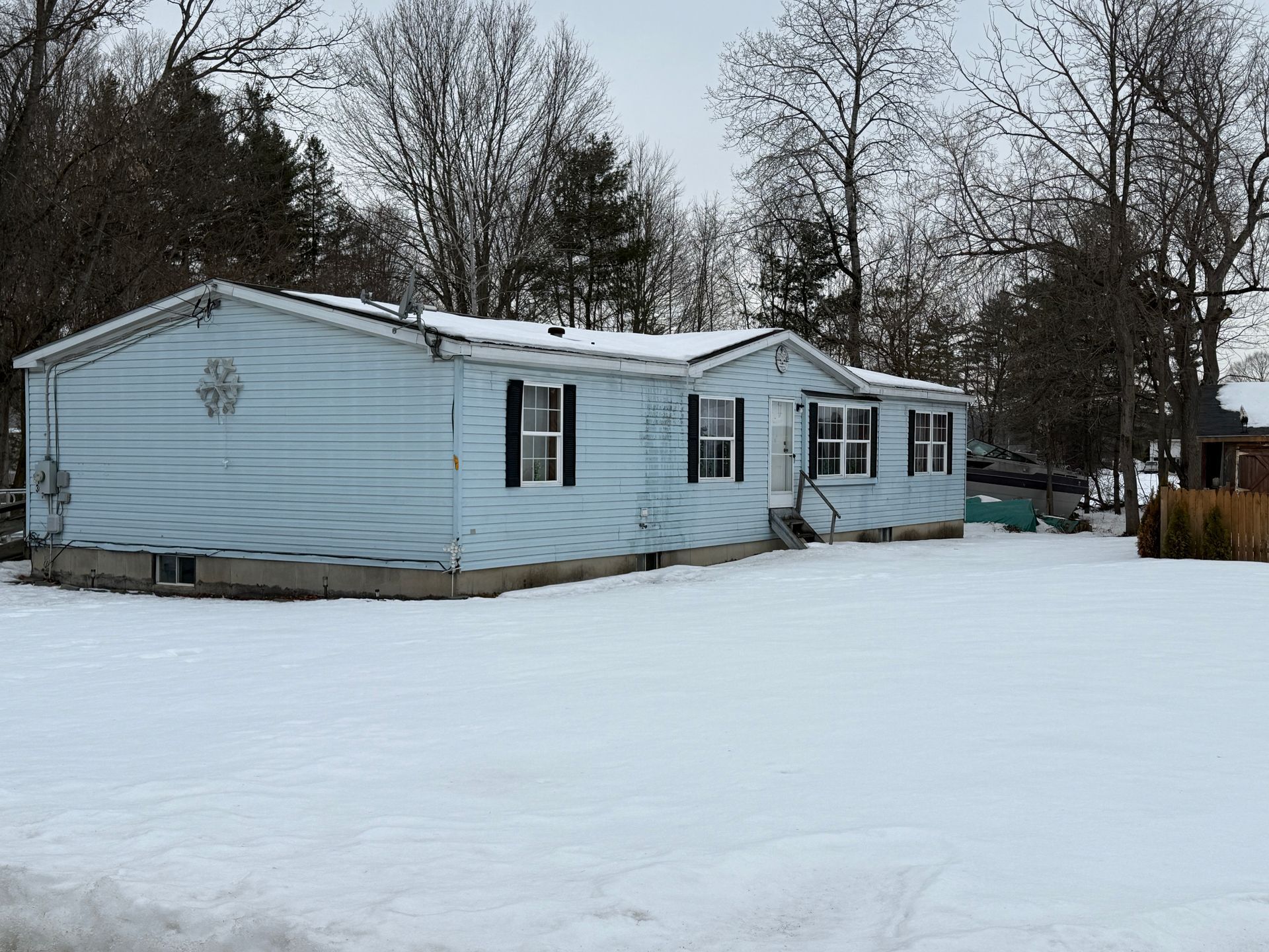 Light blue ranch-style house with black shutters, in a snow-covered yard with bare trees in the background.