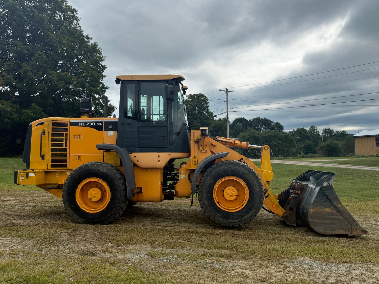 Yellow front loader with bucket parked on a gravel lot under cloudy skies