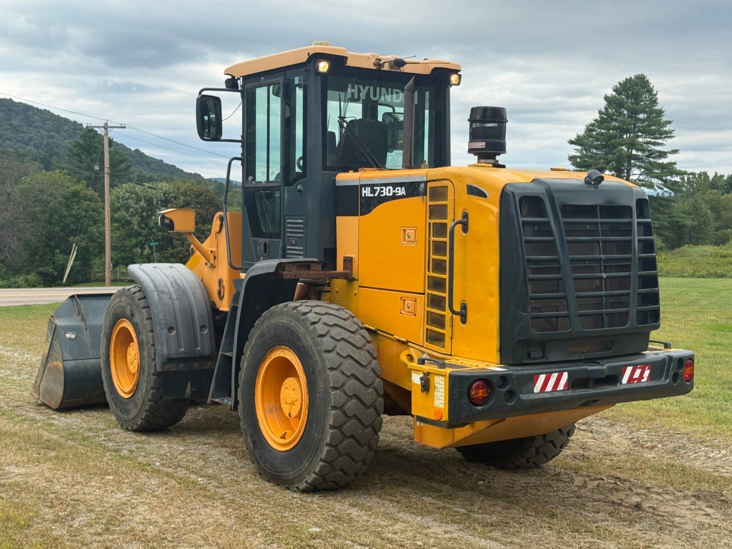 Yellow wheel loader parked on grass with mountains and trees in the background