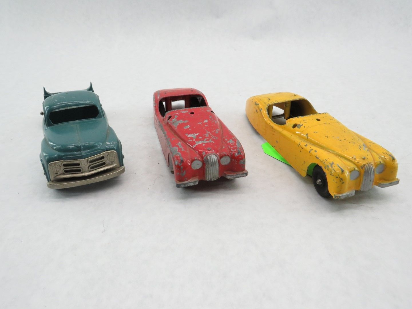 Three vintage toy cars: green truck, red car, yellow convertible.