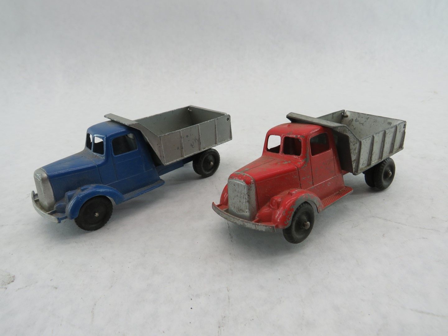 Two toy dump trucks, one blue, one red, side-by-side on a white surface. Antique.