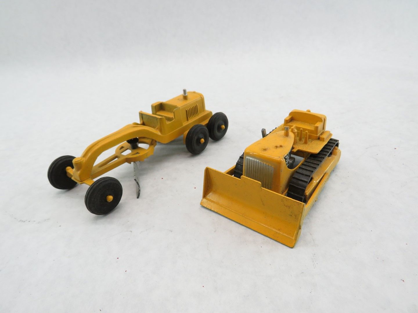Two yellow toy construction vehicles: a grader and a bulldozer. Antique.