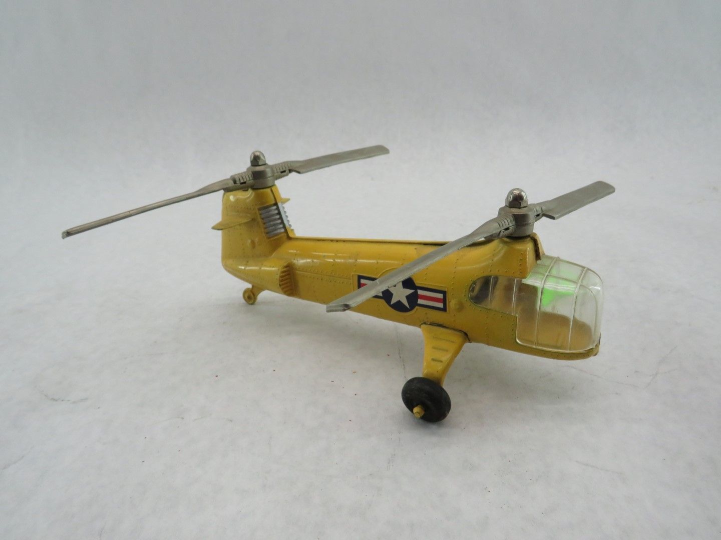 Yellow toy helicopter with dual rotors, black wheels, and a U.S. flag symbol on its side. Antique.