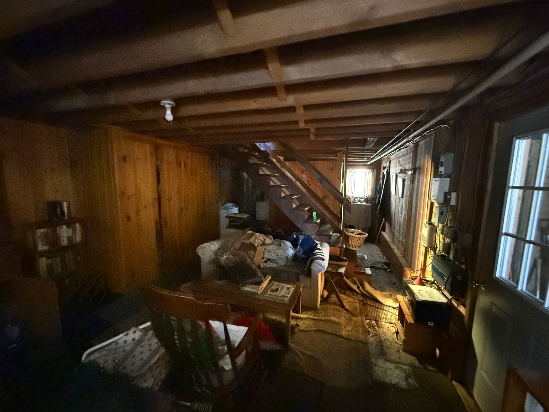 Basement with wooden walls, stairs, and a window. Various furniture and items.
