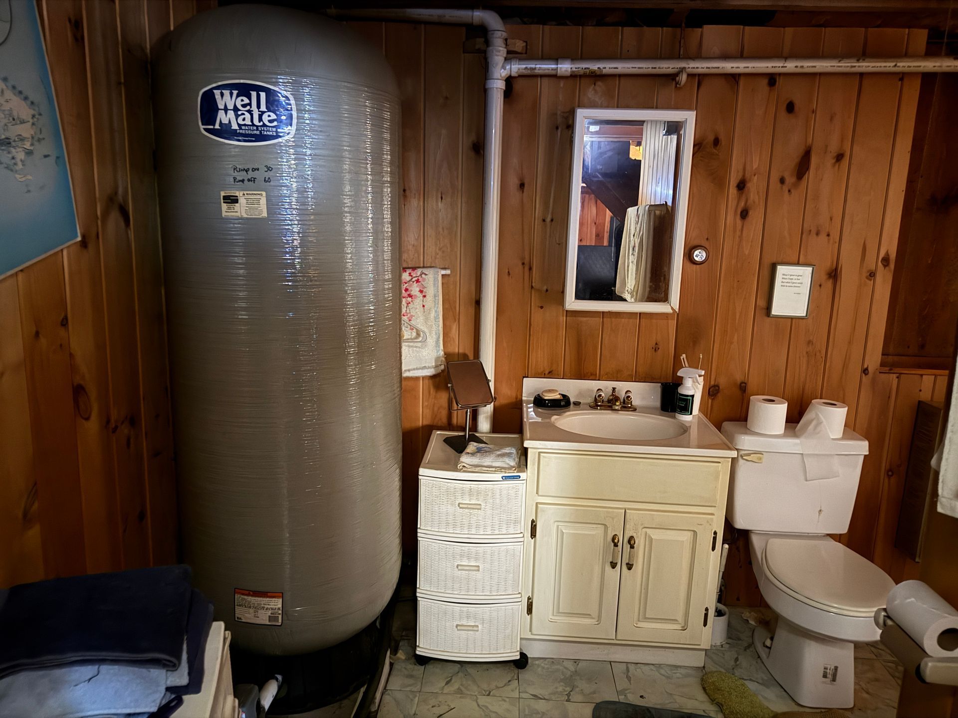 Bathroom with a water tank, sink, toilet, and wooden walls.