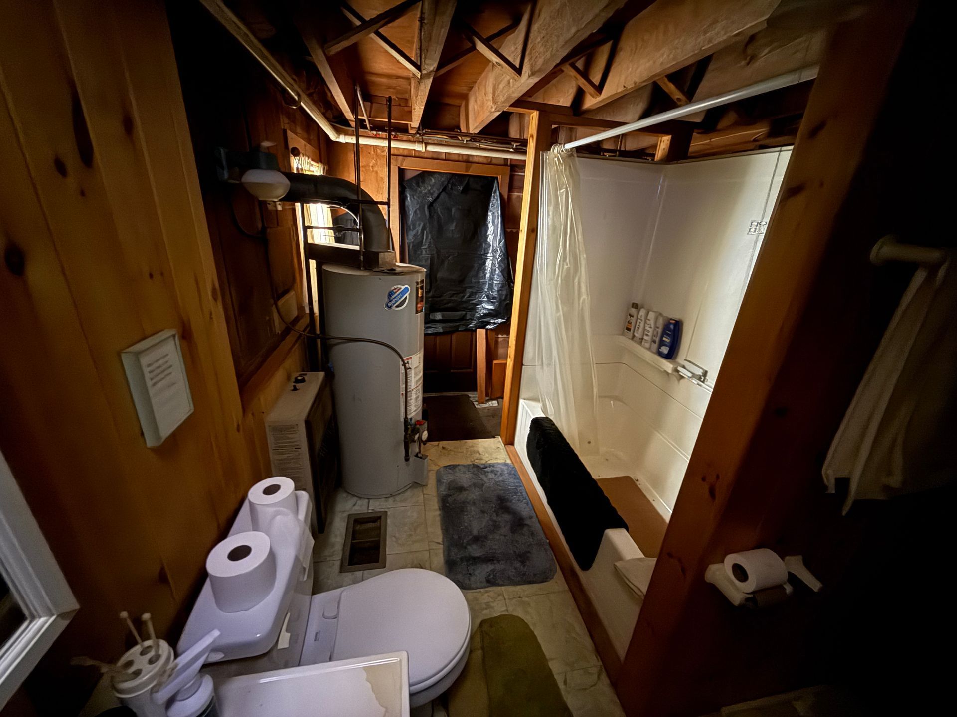 Bathroom with wood paneling, a toilet, water heater, shower, and toilet paper.