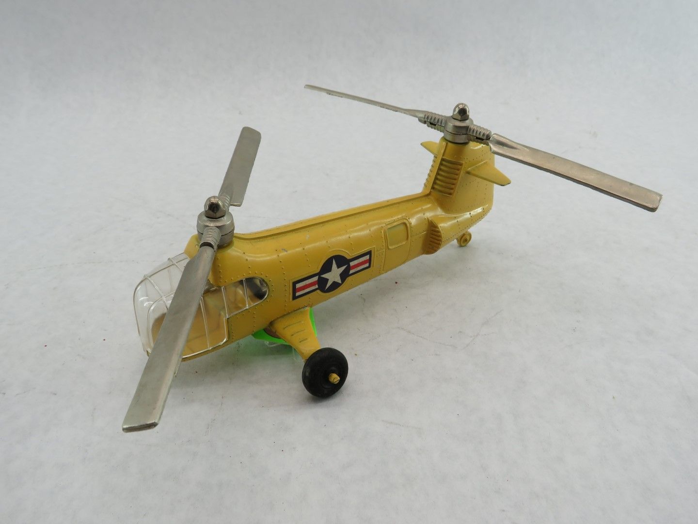 Yellow toy helicopter with dual rotors and black wheel. A USA star emblem is visible. Antique.