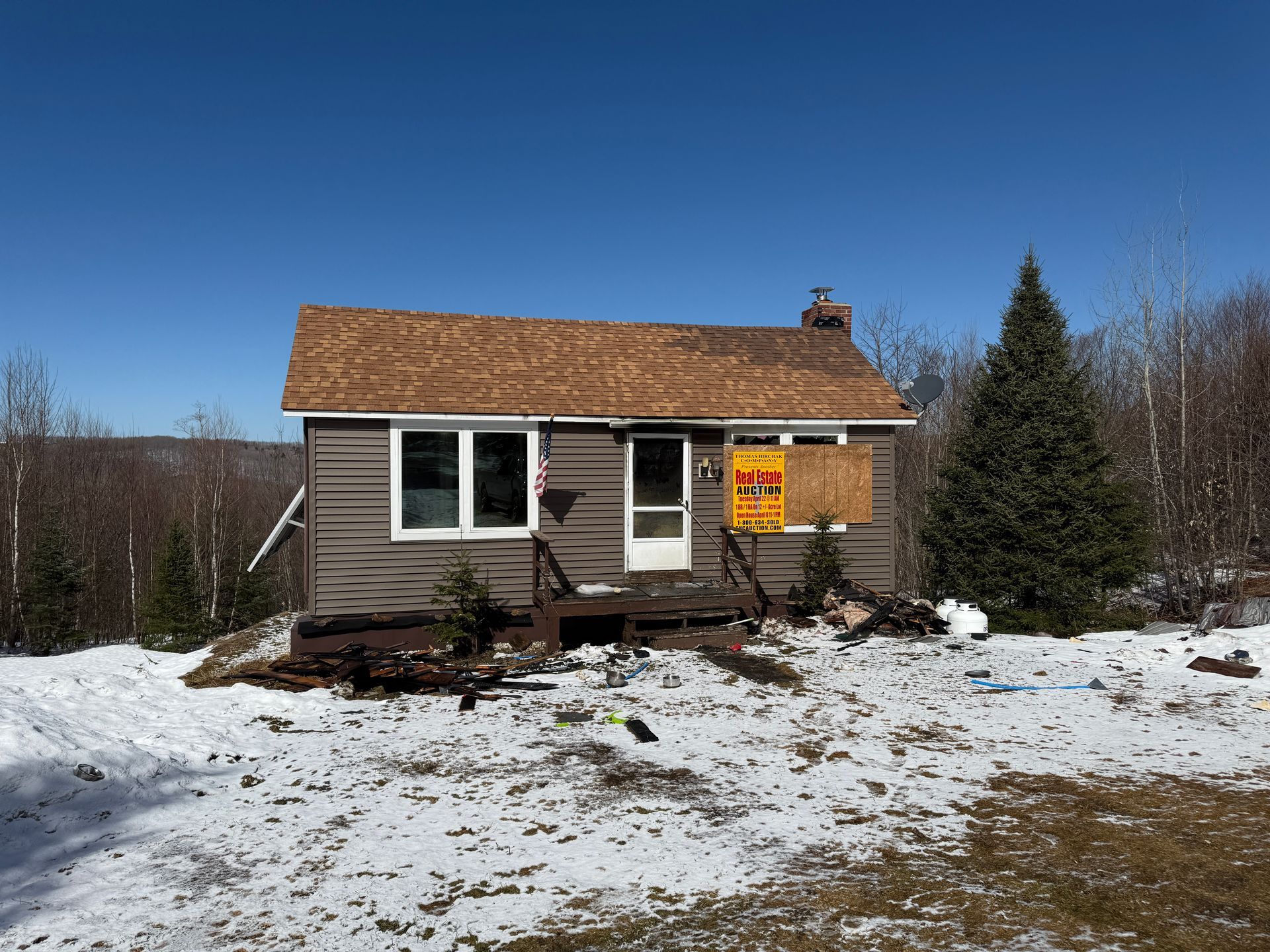 Small, brown cabin with windows, on a snow-covered hill under a blue sky.