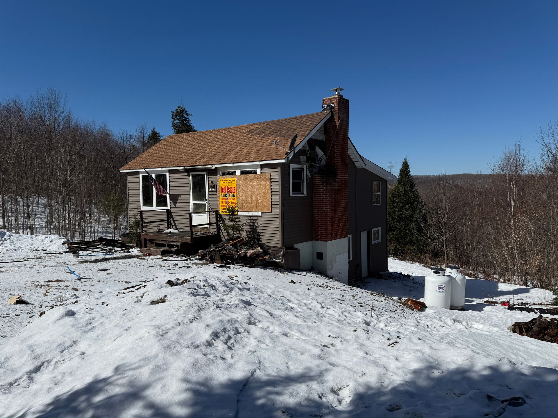 Small house with windows, brick chimney, snow-covered ground, and a clear blue sky.