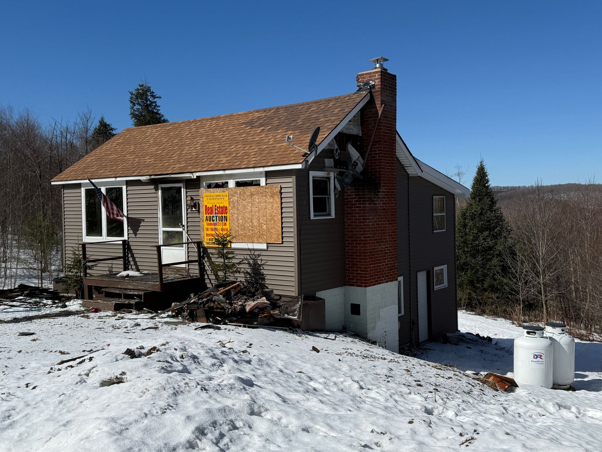 House with boarded-up window, chimney, and snow-covered ground.