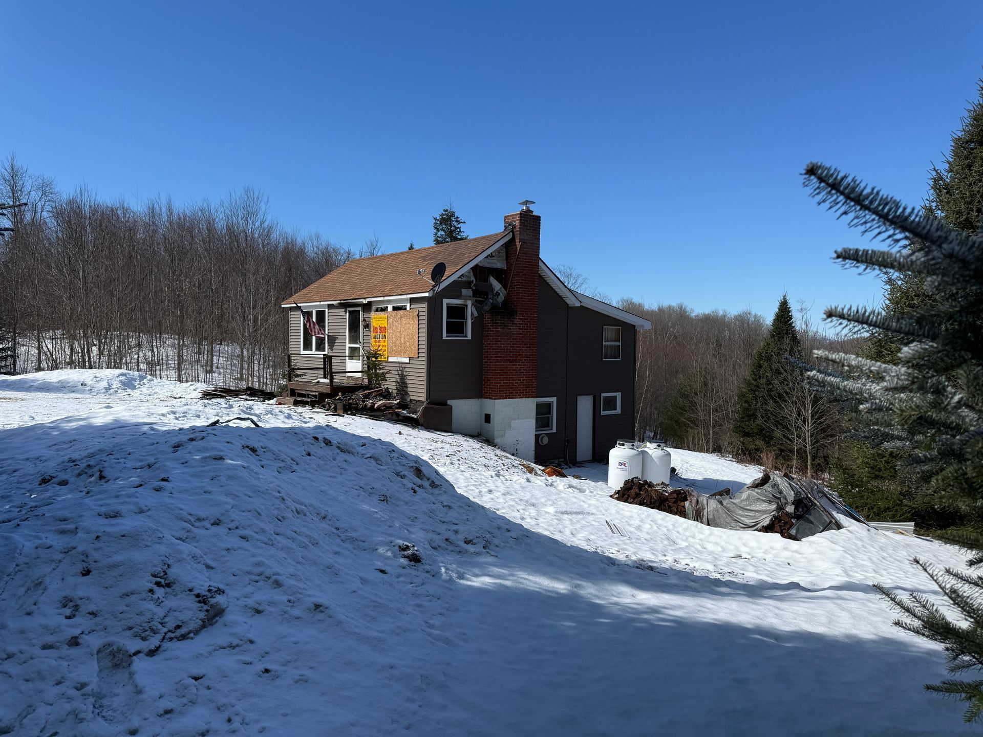 House with snow-covered yard, brick chimney, clear blue sky, and trees in the background.