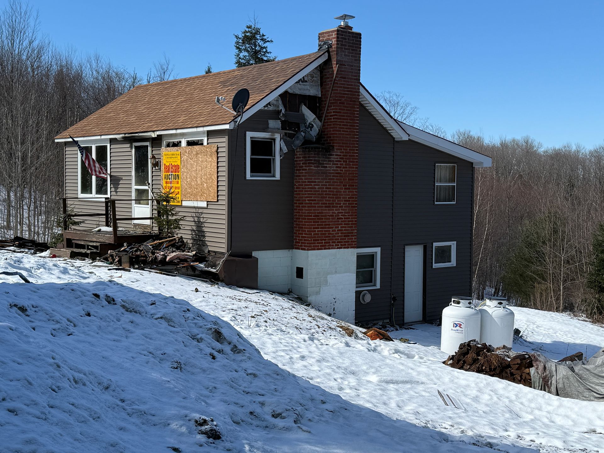 House with chimney, wall, and roof. Snowy ground and forest in the background.