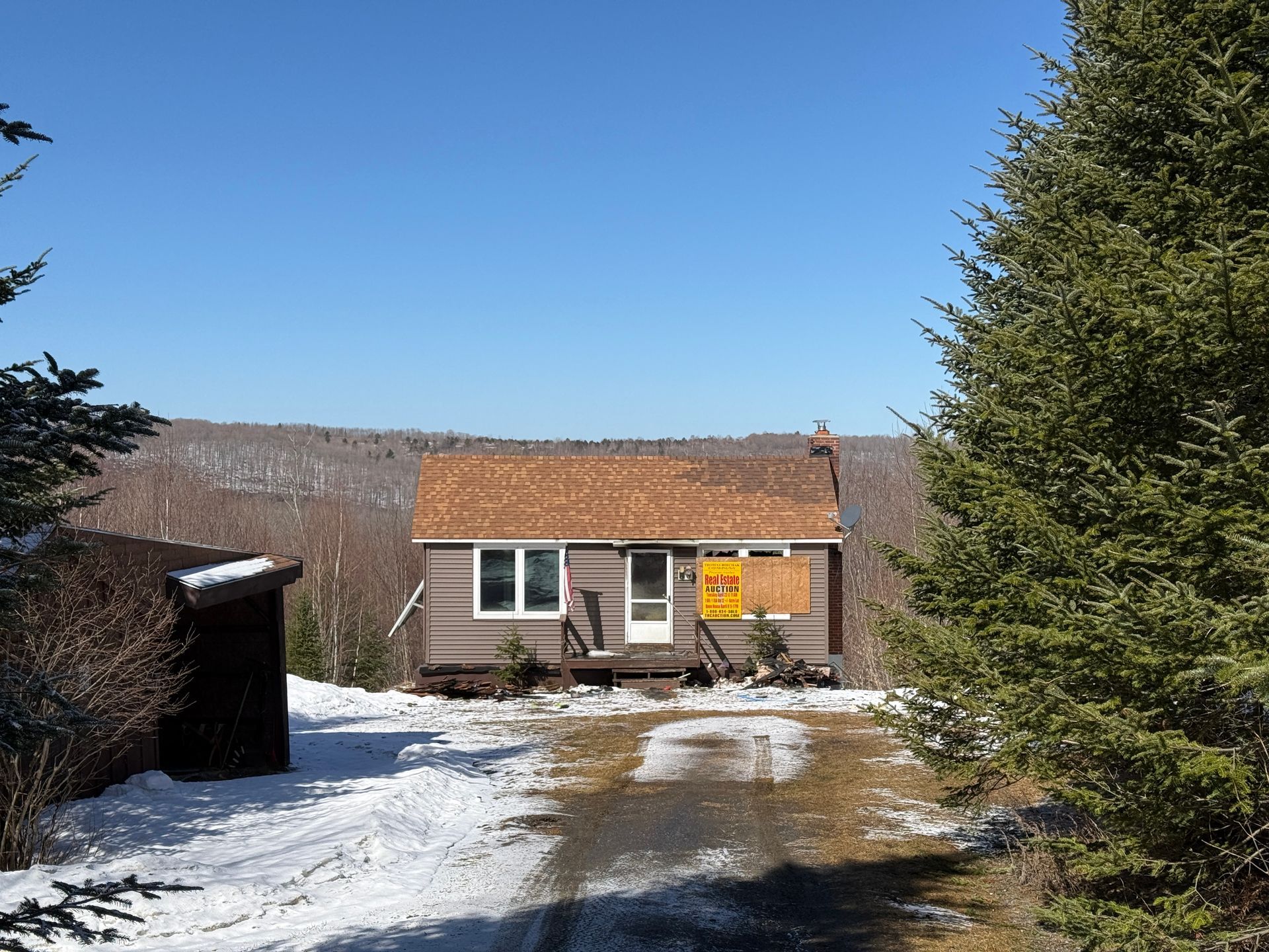 Brown cabin in a snowy setting with trees and a blue sky.