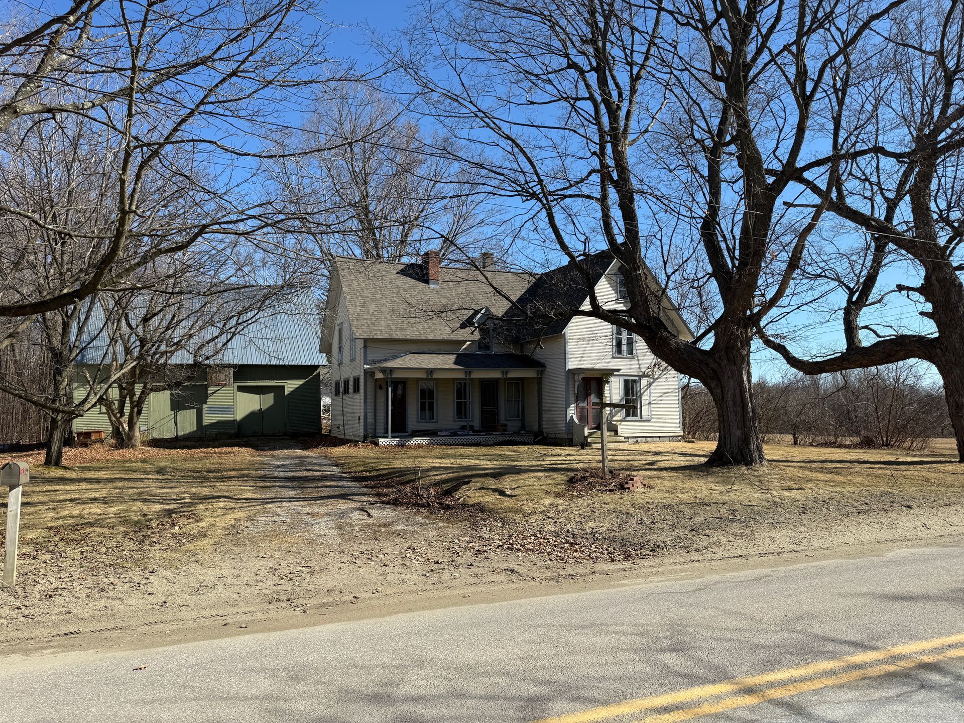 House with porch, bare trees in front. Road in foreground.