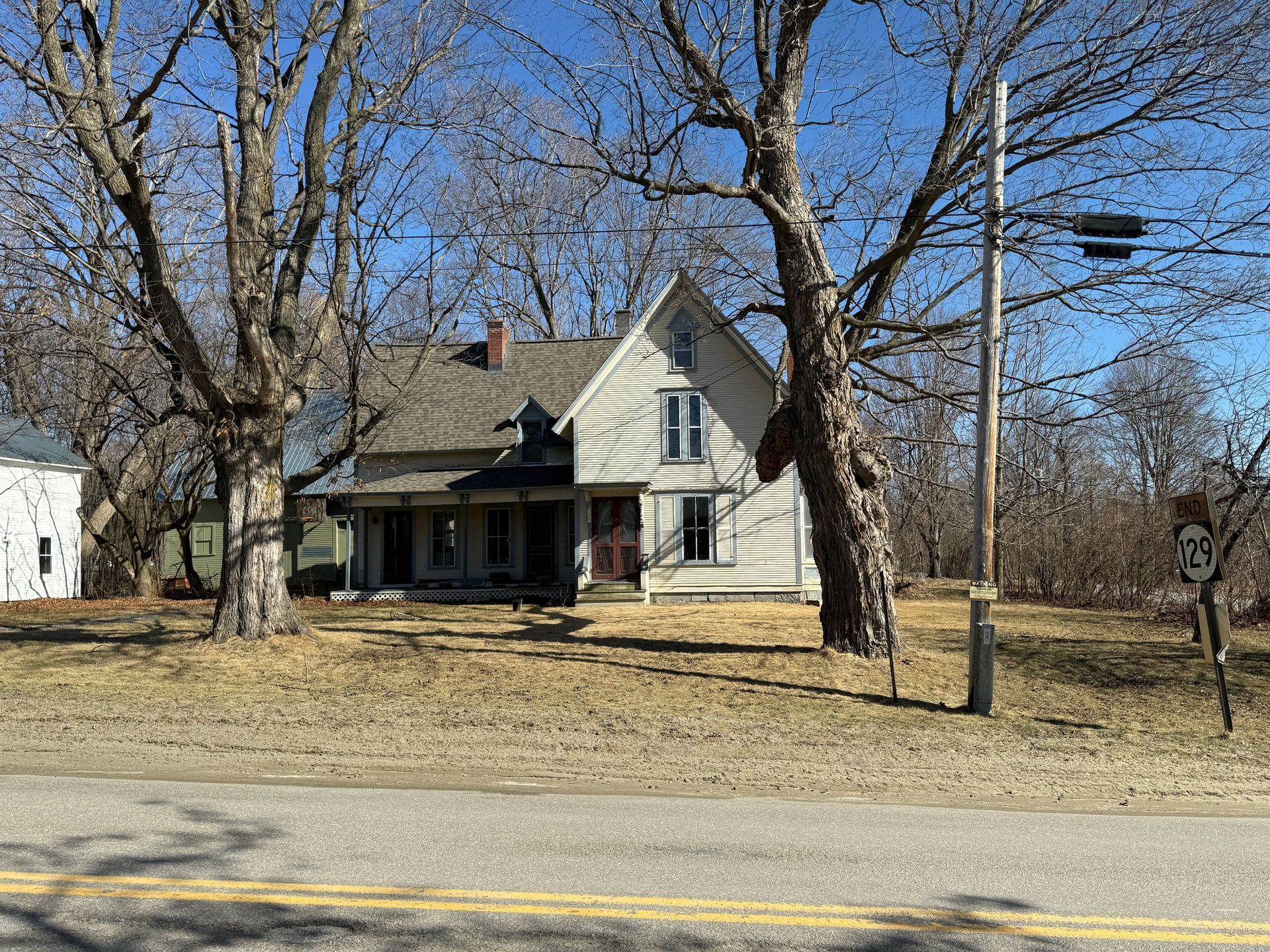 Two-story house with roof, trees on either side, and road in front.