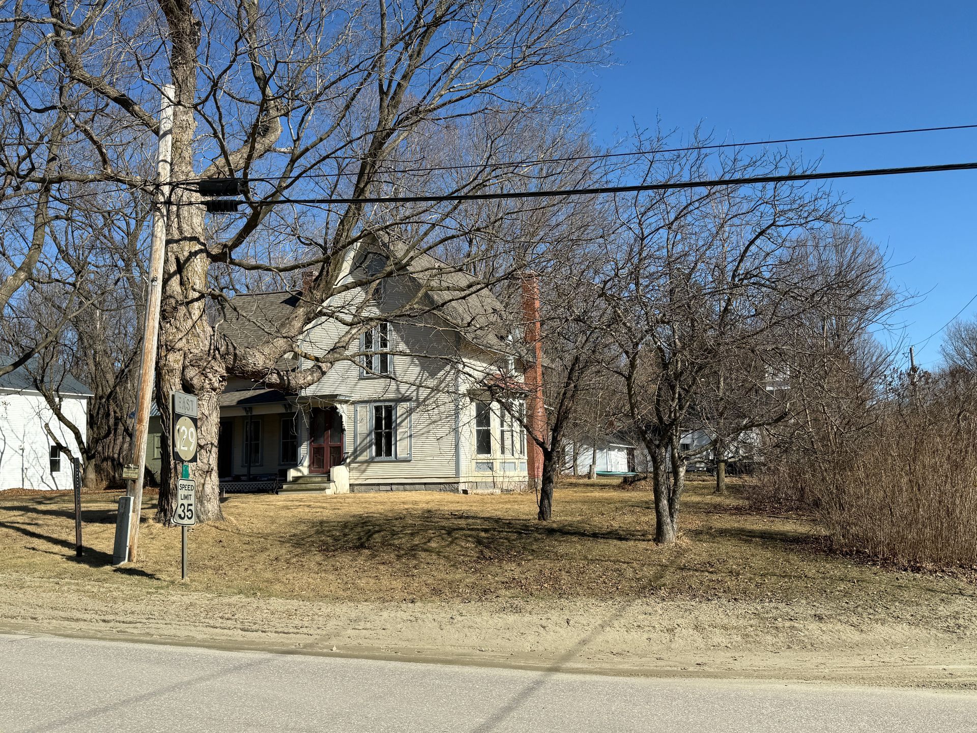 White, two-story house with a prominent roofline, set among bare trees on a sunny day.