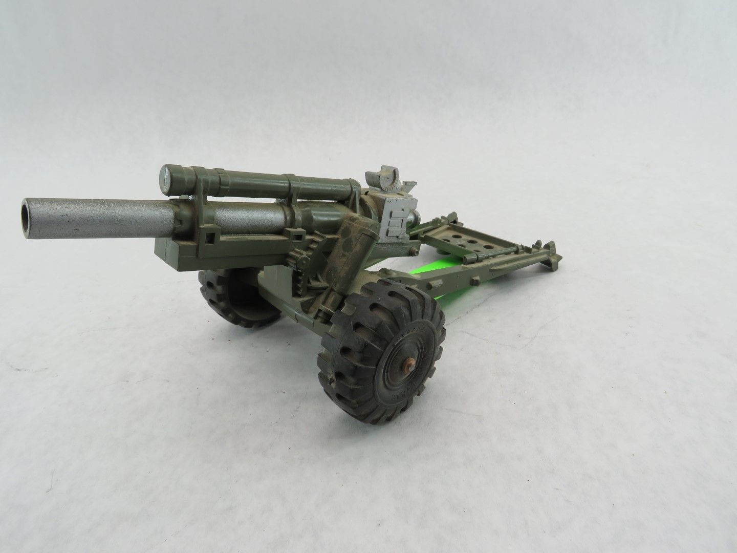 A toy army-green cannon with a textured silver barrel and black wheels, against a white background. Antique.