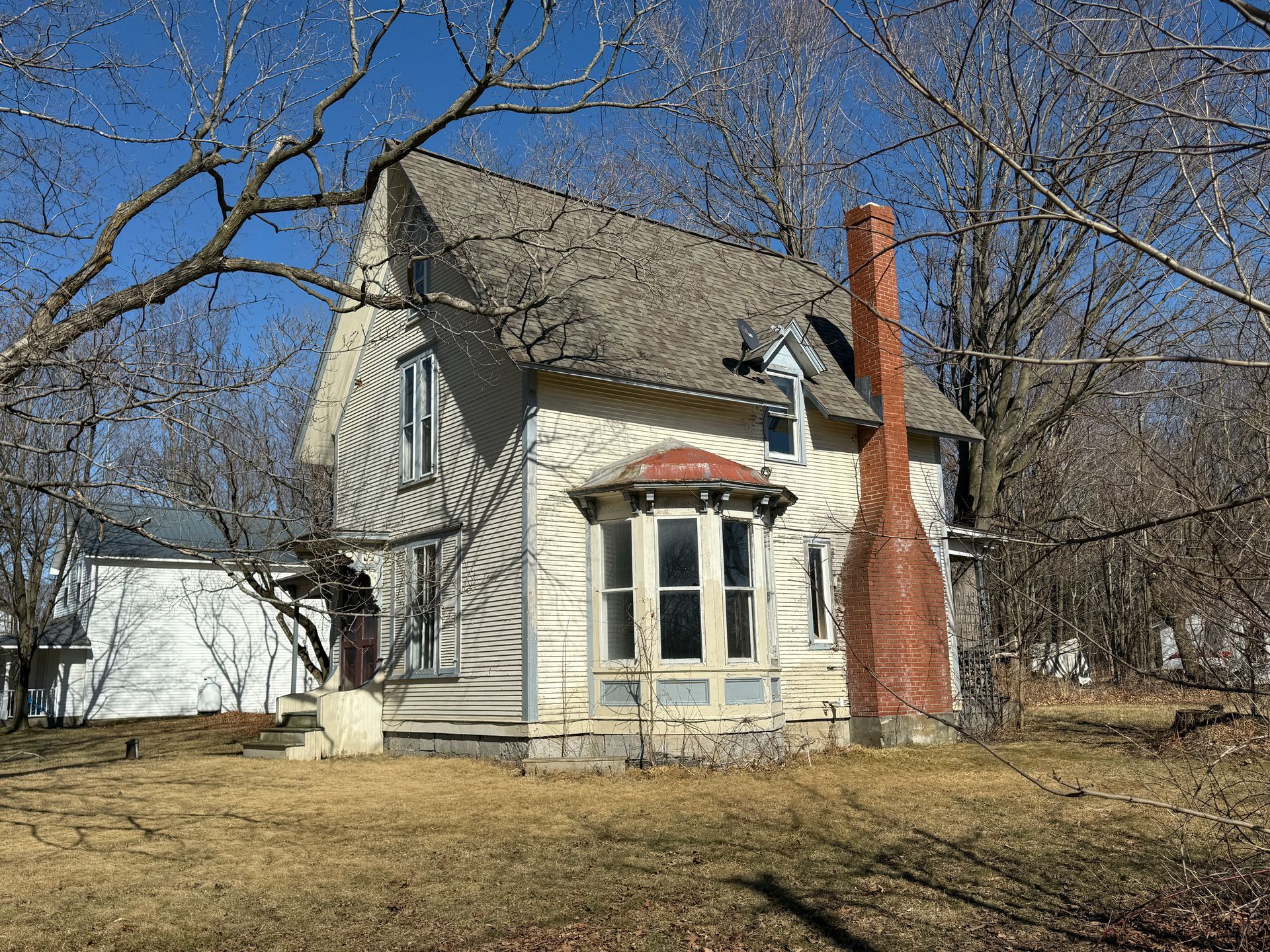 Two-story house with a prominent brick chimney and bay window.