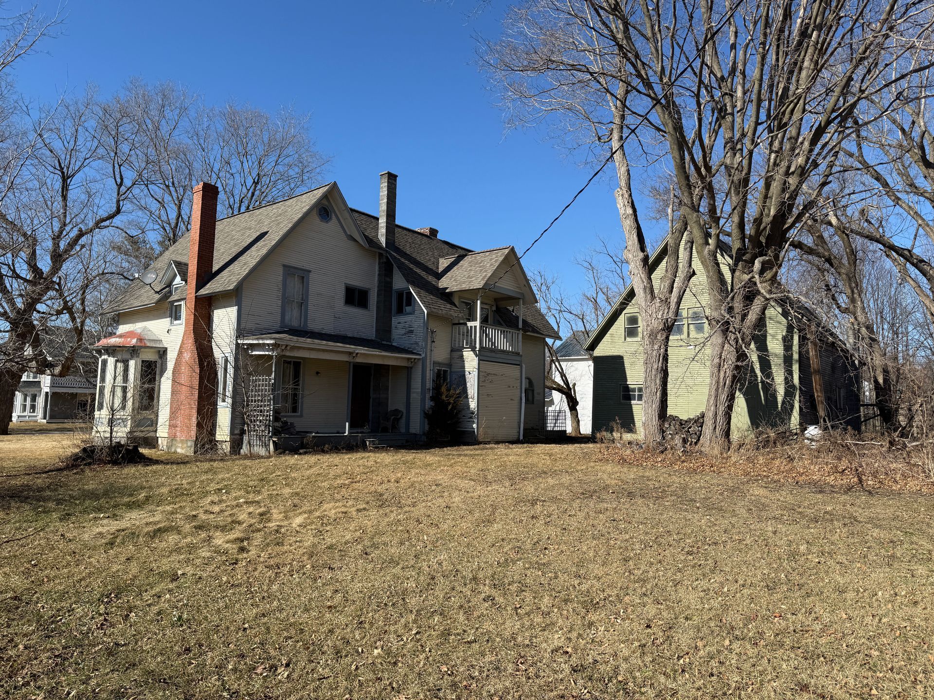 House with a brick chimney and a yard with bare trees under a blue sky.