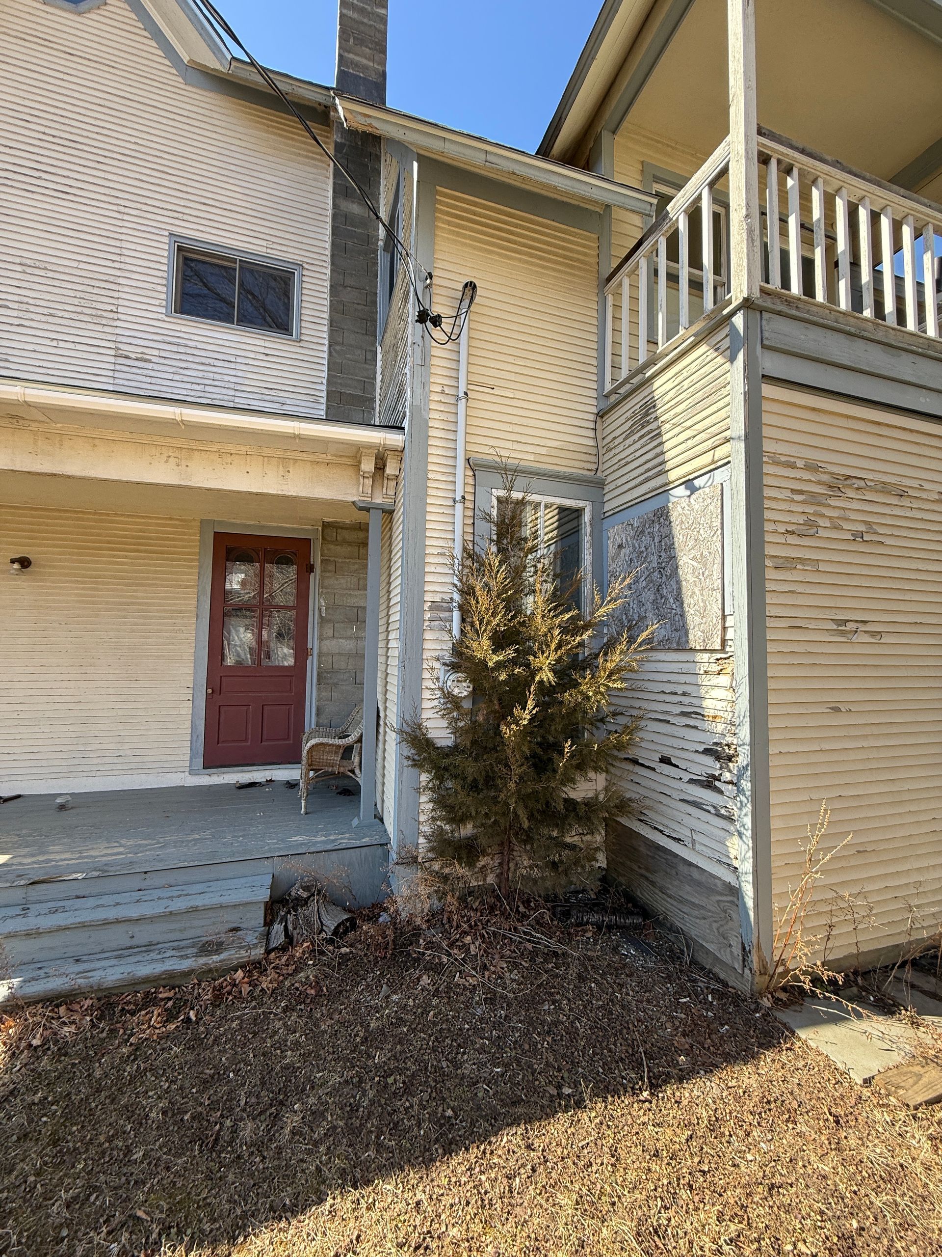 Exterior view of an old house with paint, porch, and a small tree in front.