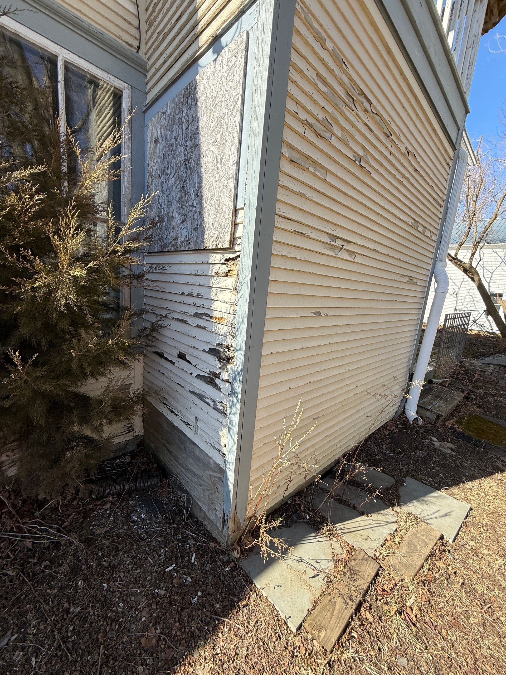 Exterior corner of a building with white paint, siding, and a downspout.