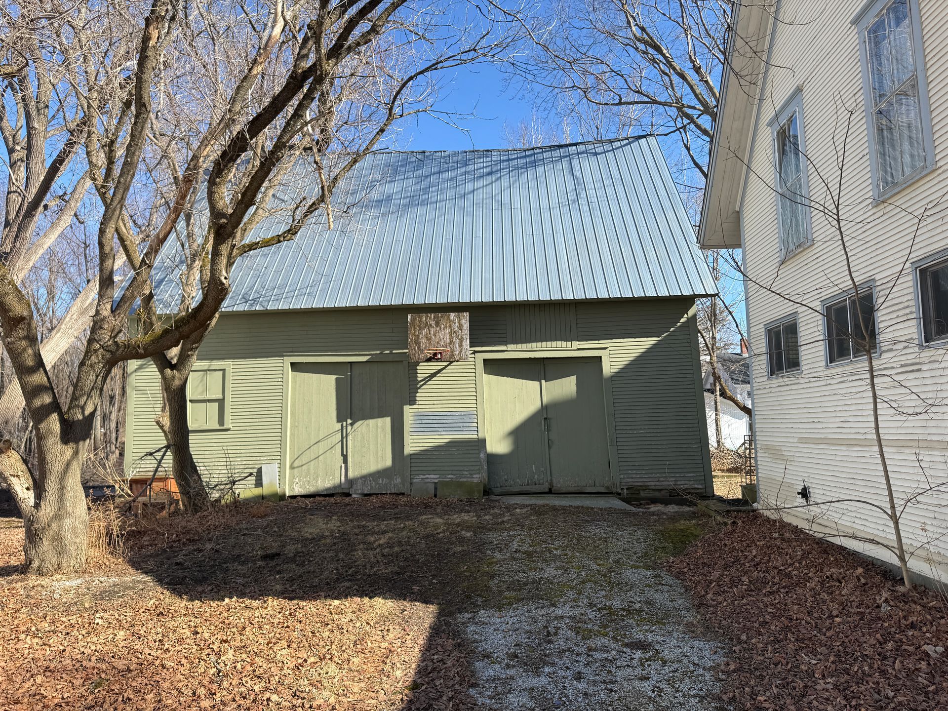 Green shed with metal roof next to a white house.