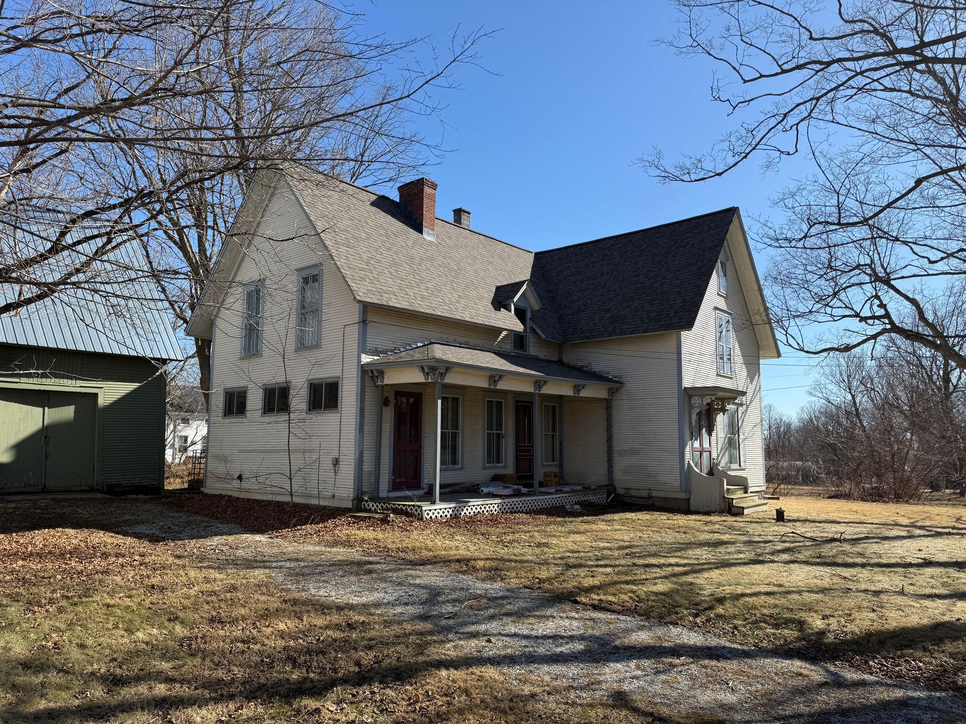 Two-story house with porch and detached green shed on a sunny day.