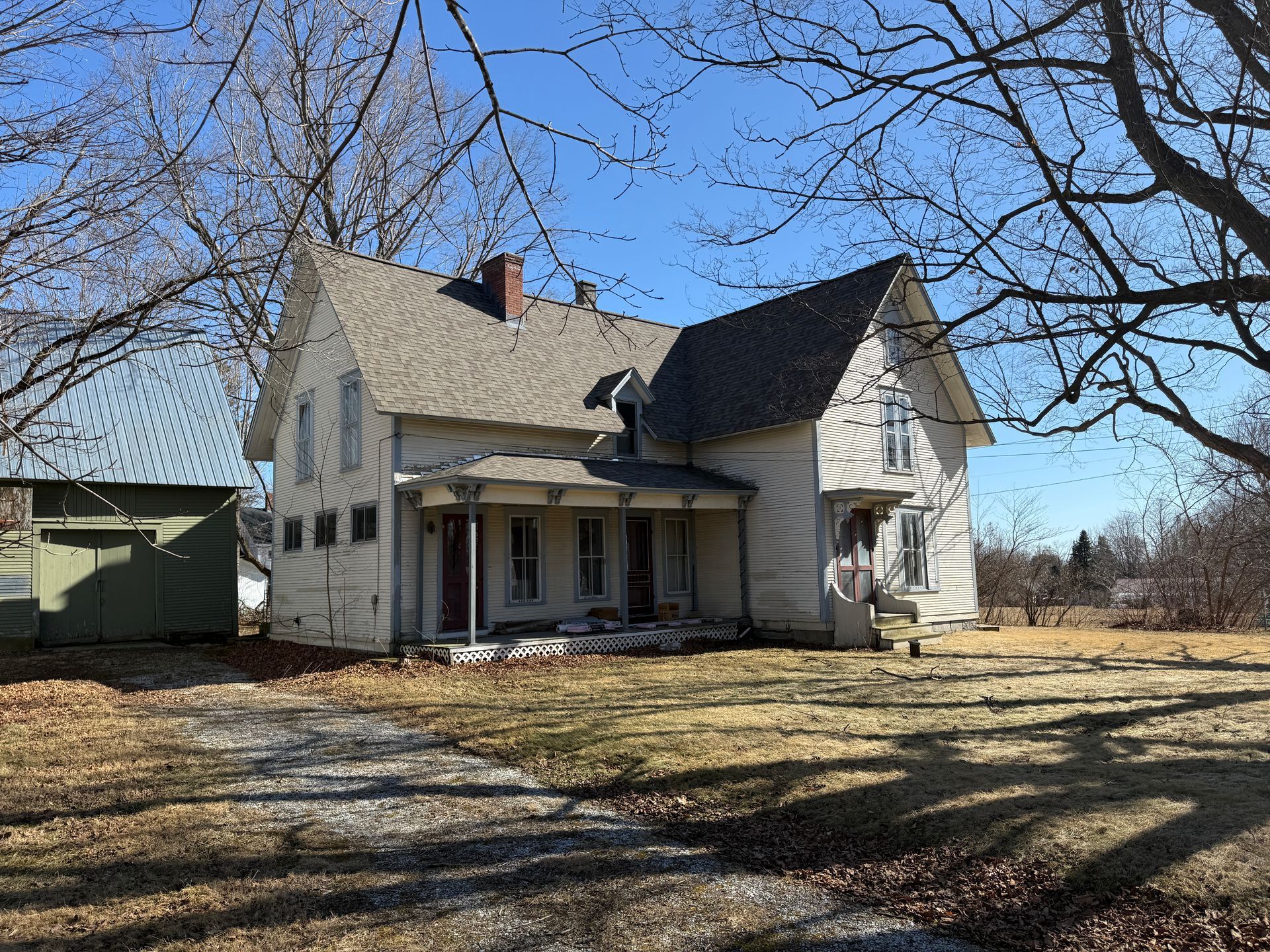 Two-story house with a porch and shed, on a sunny day with bare trees.