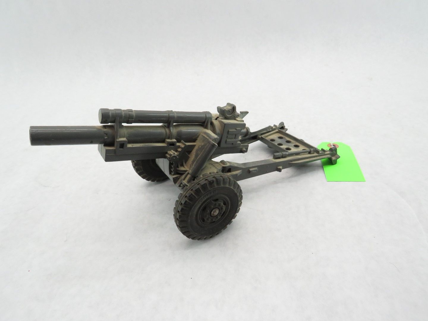 A dark green artillery gun with two wheels and a tow bar, set on a white surface. Antique.
