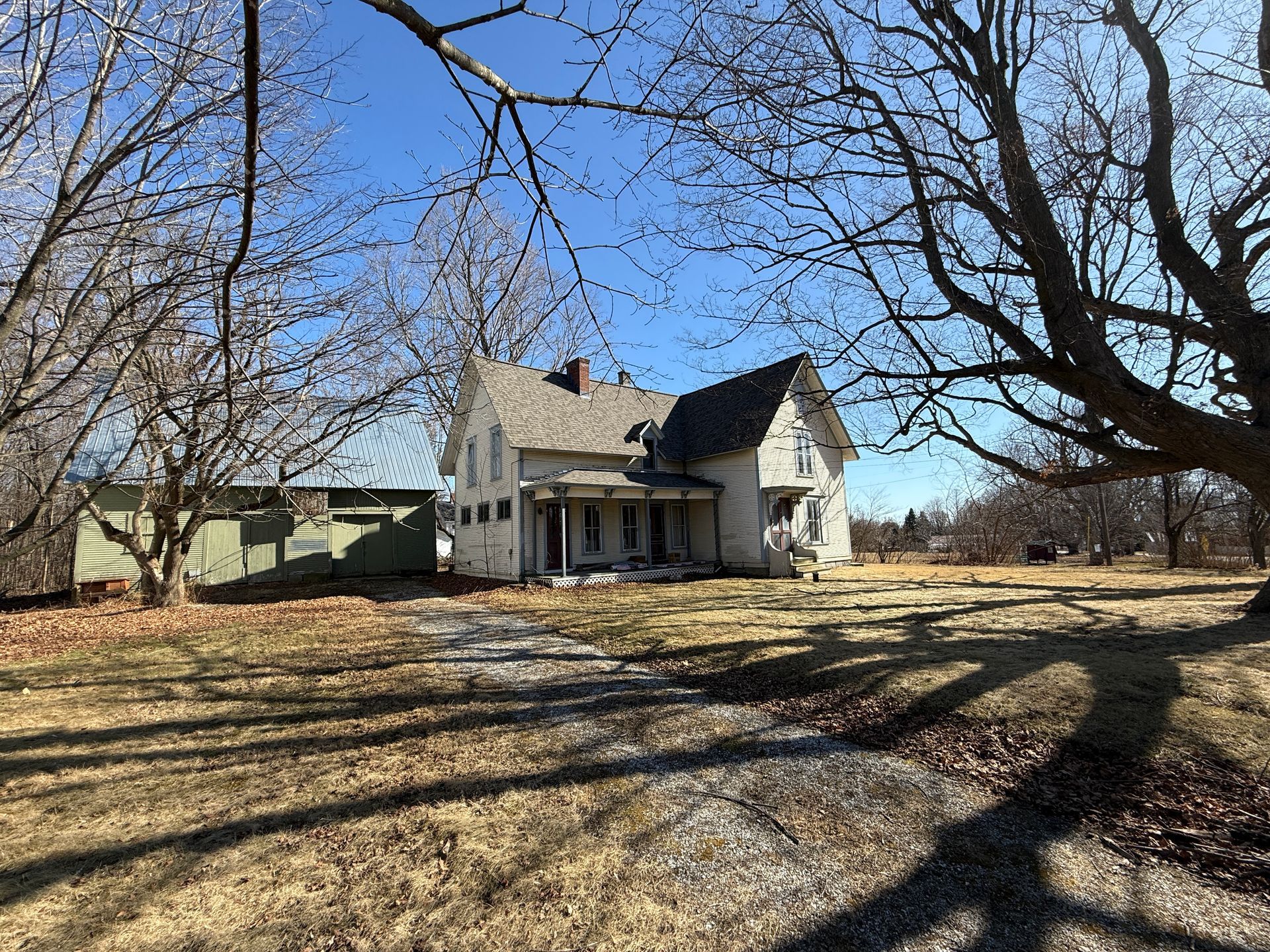 Two-story house with a porch and detached shed on a sunny, grassy lot.