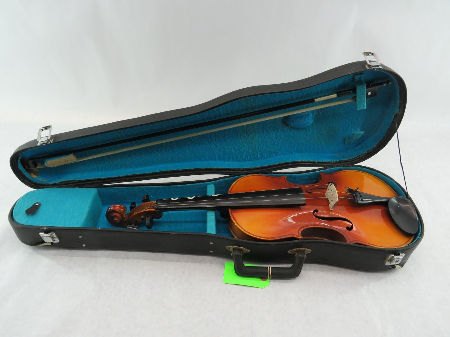 Violin in open black case with blue interior; bow at top, instrument inside.