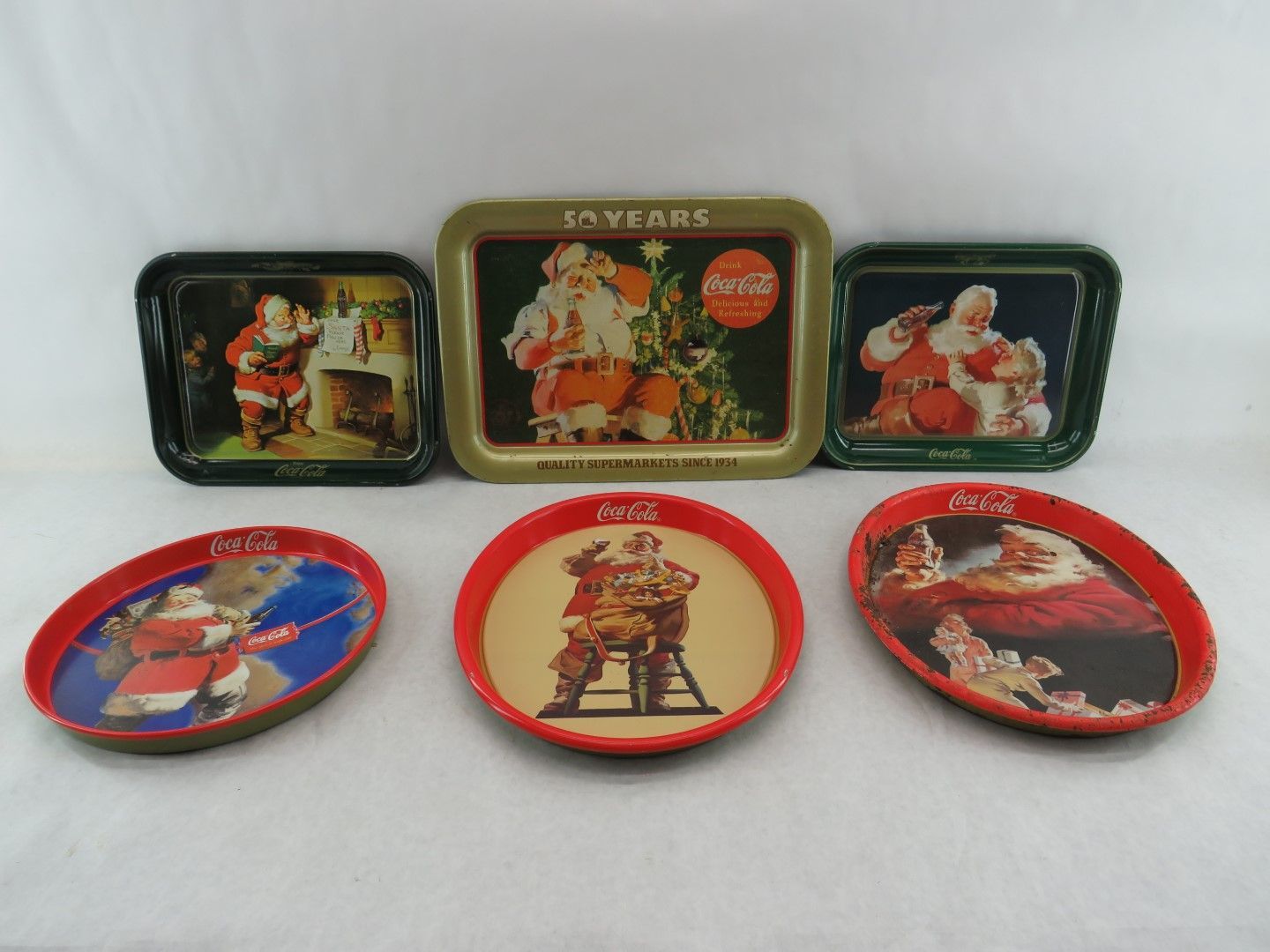 Six vintage Coca-Cola Santa trays. Rectangular and oval shapes. Festive images, red, green, and gold colors.
