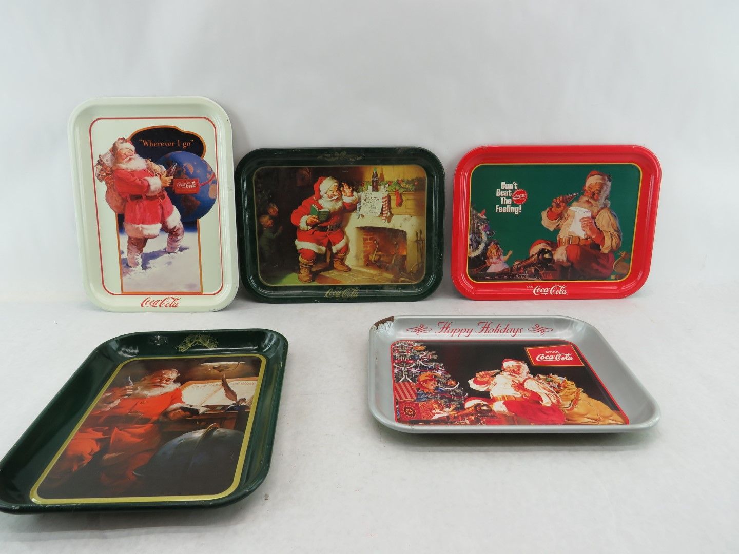 Five vintage Coca-Cola trays with Santa Claus designs, featuring different scenes and colors.