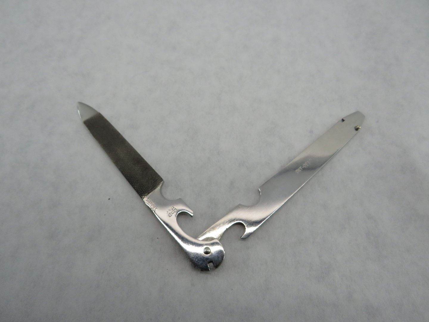 Silver pocket tool with a nail file, bottle opener, and blade, open on a white surface.