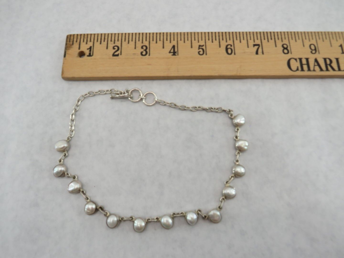 Silver bracelet with tear-drop shaped beads next to a wooden ruler.
