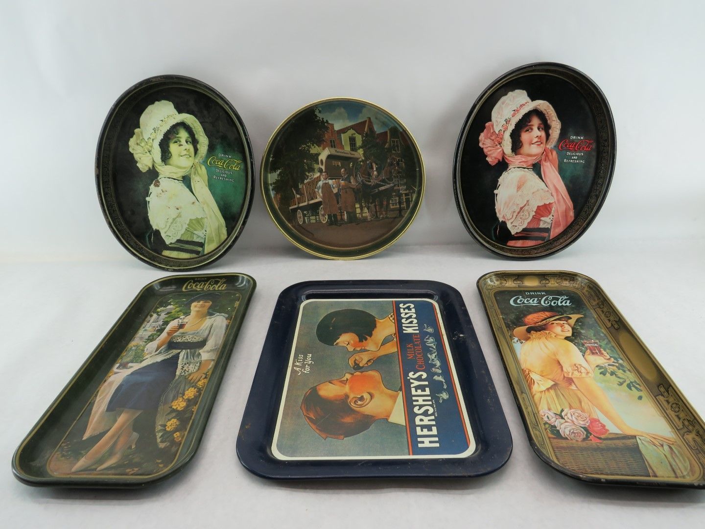 Six vintage metal advertising trays: Coca-Cola, Hershey's, and portraits of women.