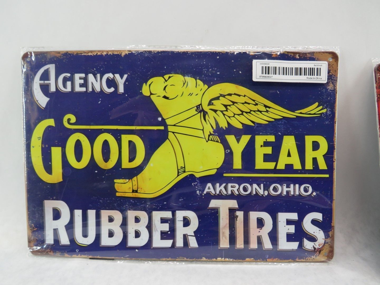 Vintage Goodyear Rubber Tires sign, blue background with yellow text and winged foot logo, weathered appearance.