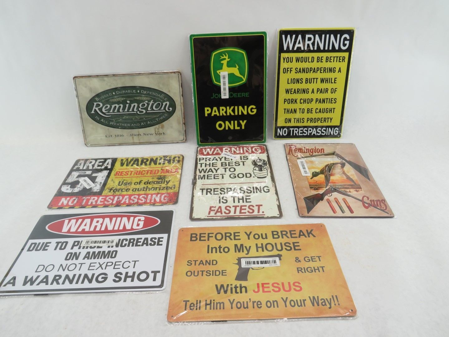 Collection of vintage-style metal signs with warning messages, including one for Remington and a John Deere parking sign.