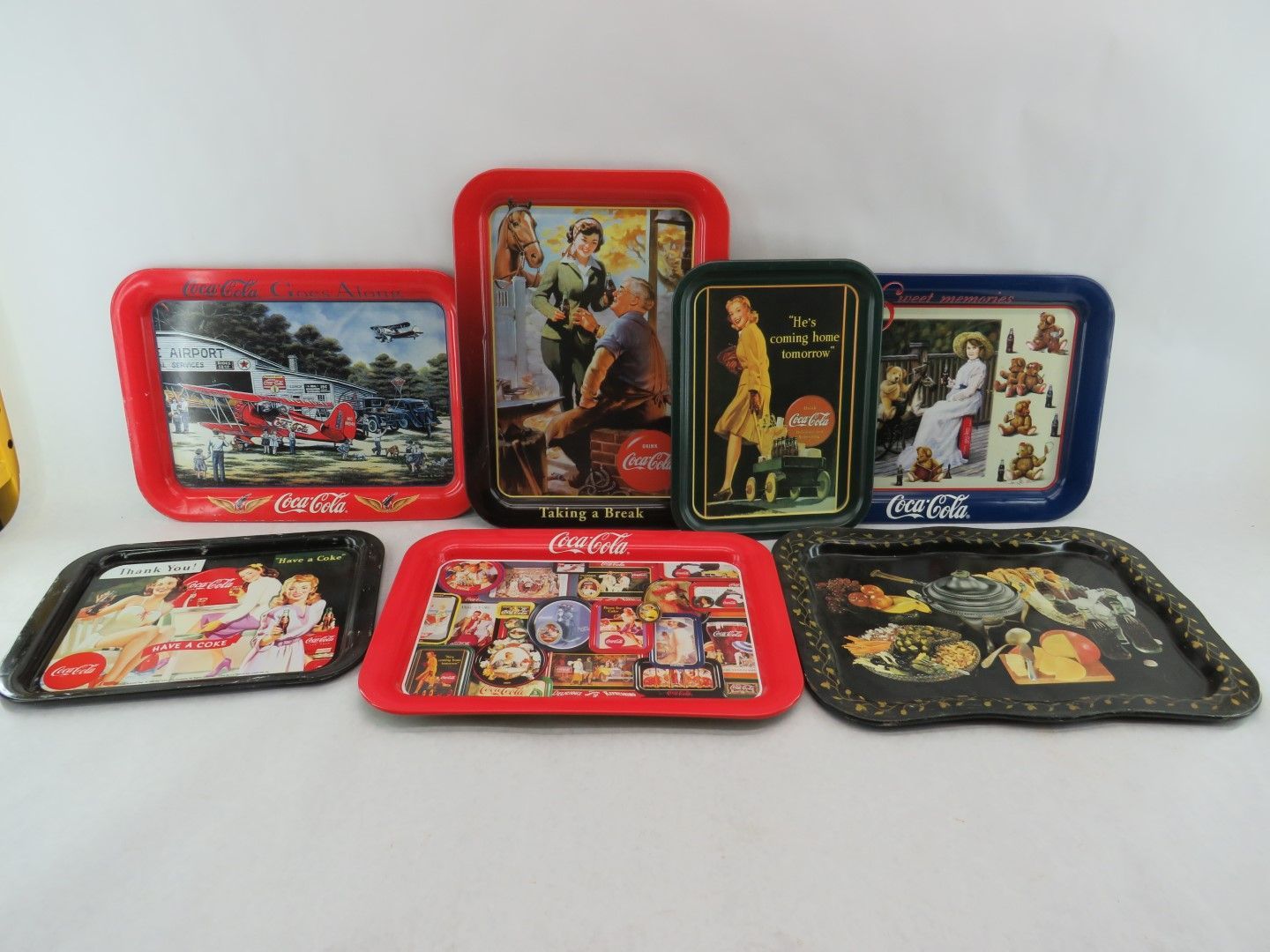 Seven vintage Coca-Cola metal serving trays with colorful advertisements, various sizes and shapes, on a white background.