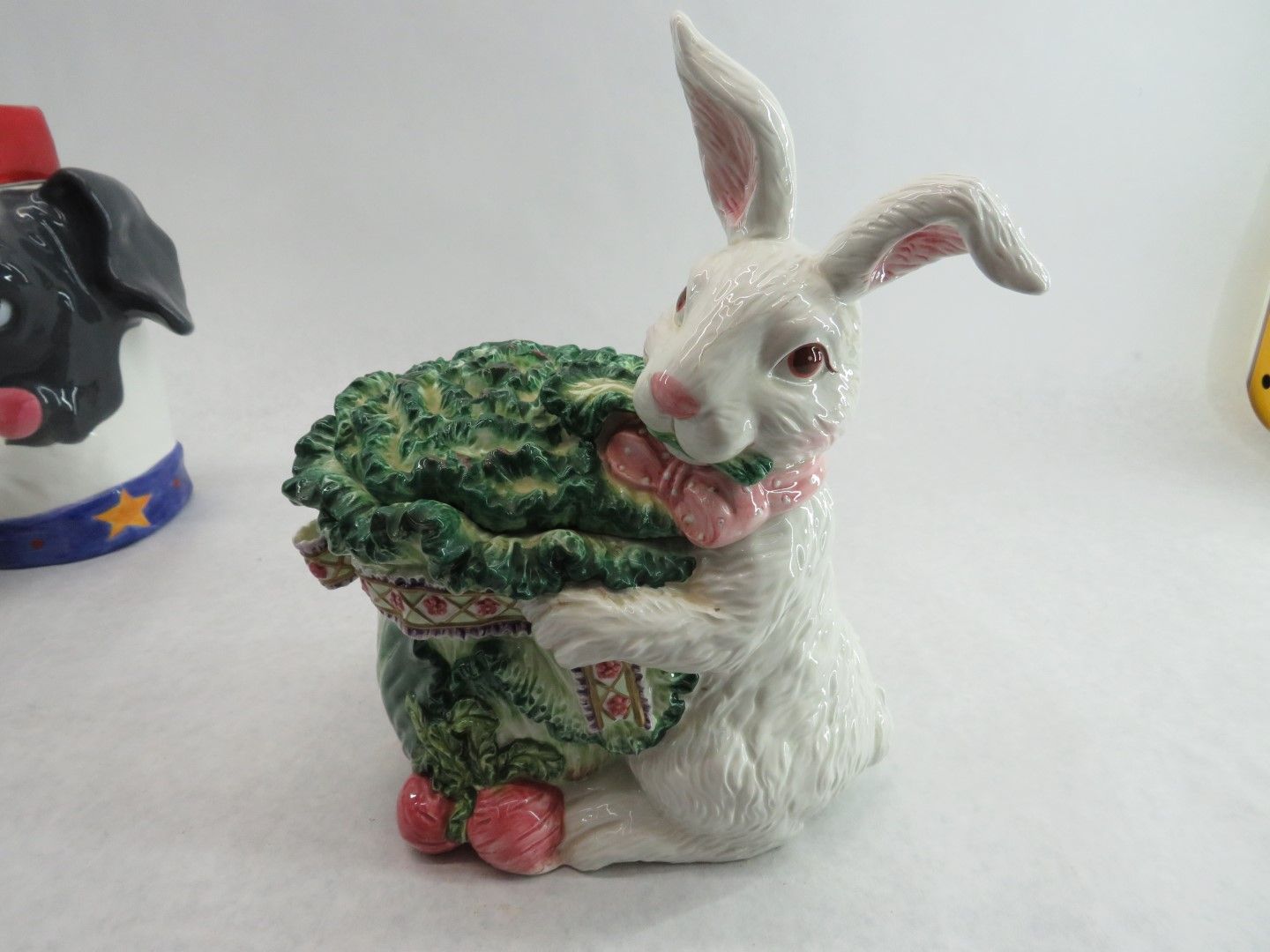 White bunny figurine holding a green cabbage, with a pink bow around its neck.