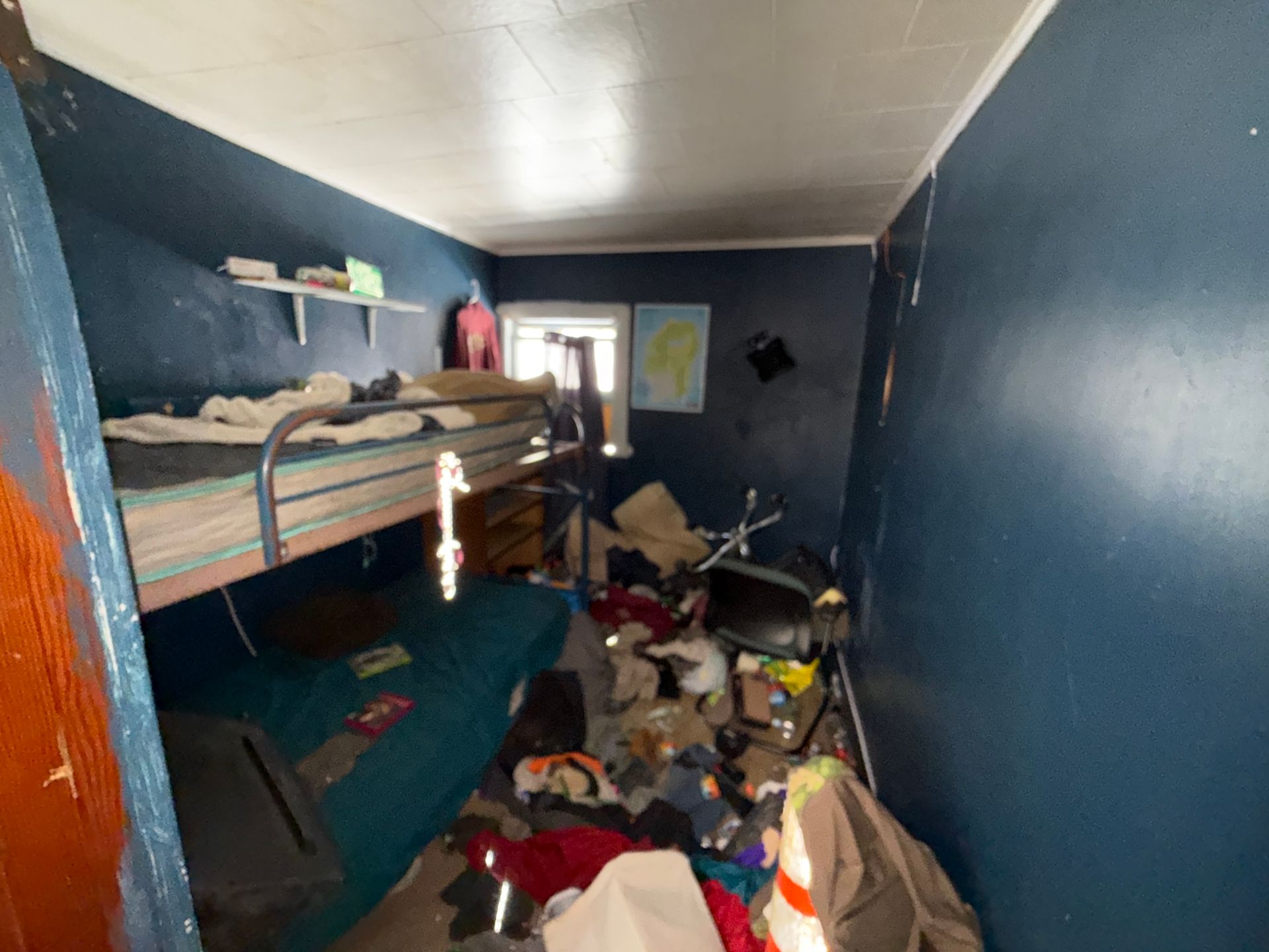A bedroom with dark blue walls, featuring a bunk bed and various items.