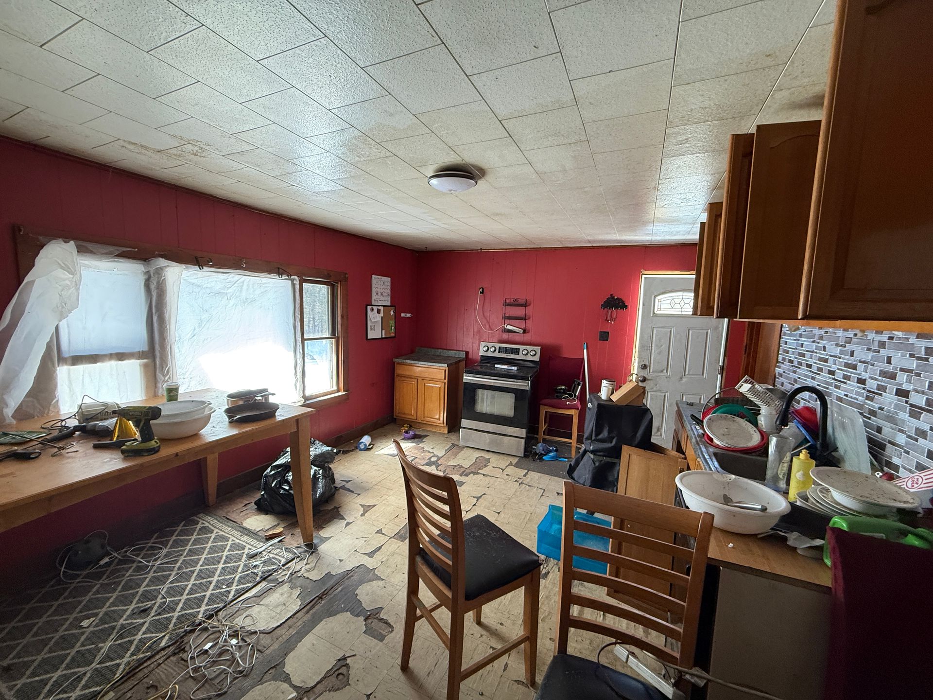 A kitchen with red walls, exposed subflooring, a wooden table, and an oven.
