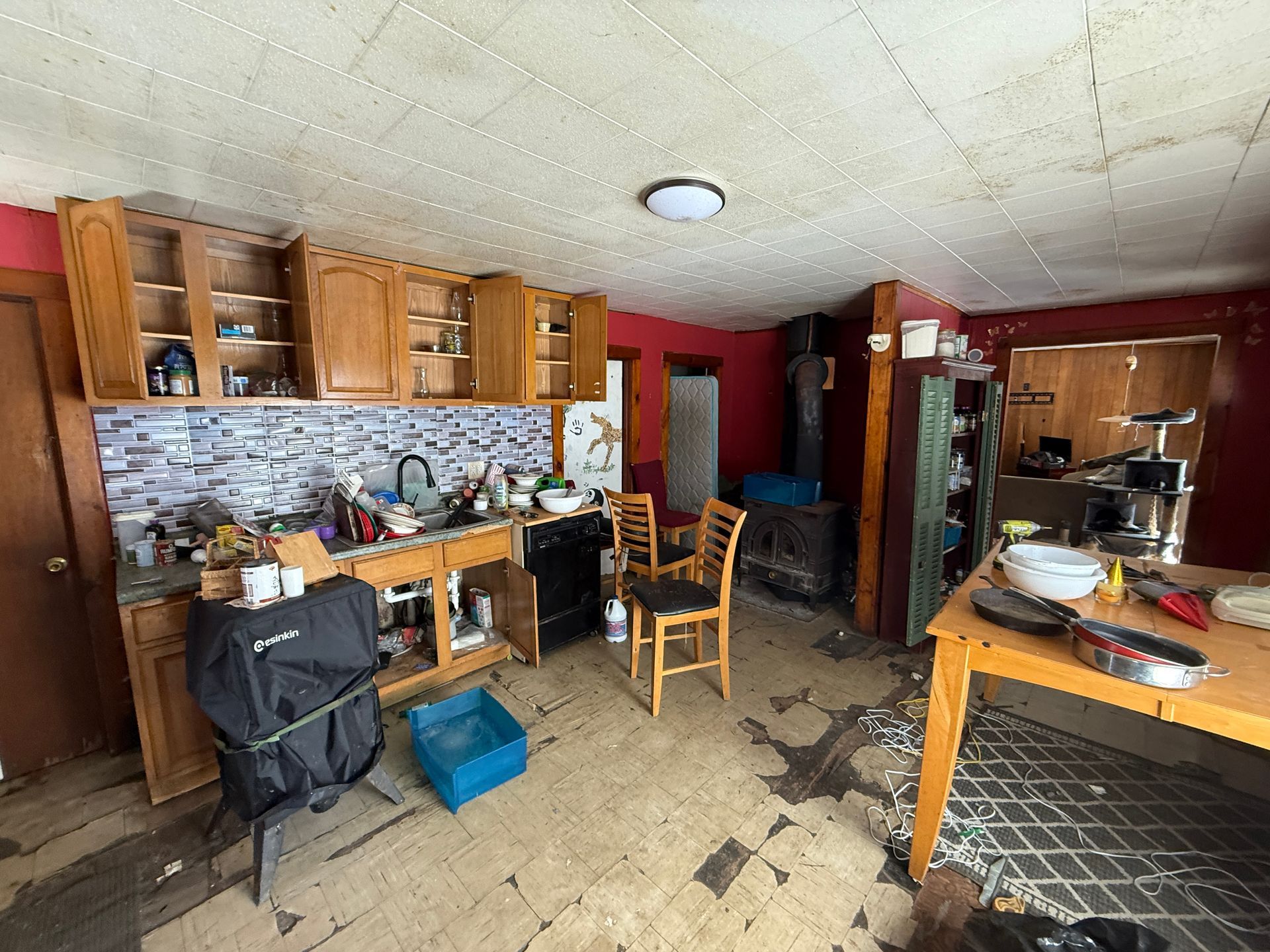 A kitchen with light wood cabinets, red walls, wooden chairs, a kitchen island, and tile flooring.